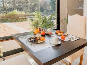 Una mesa de comedor con alimentos para el desayuno, una planta y vistas al exterior.