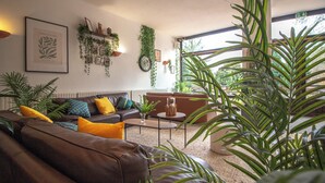 A living room with a brown leather sofa, a coffee table, and a large window with plants. - Garden & City Capvern-les-Bains (Capvern)