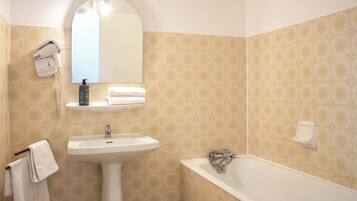 A bathroom with a sink, mirror, hairdryer, and bathtub.