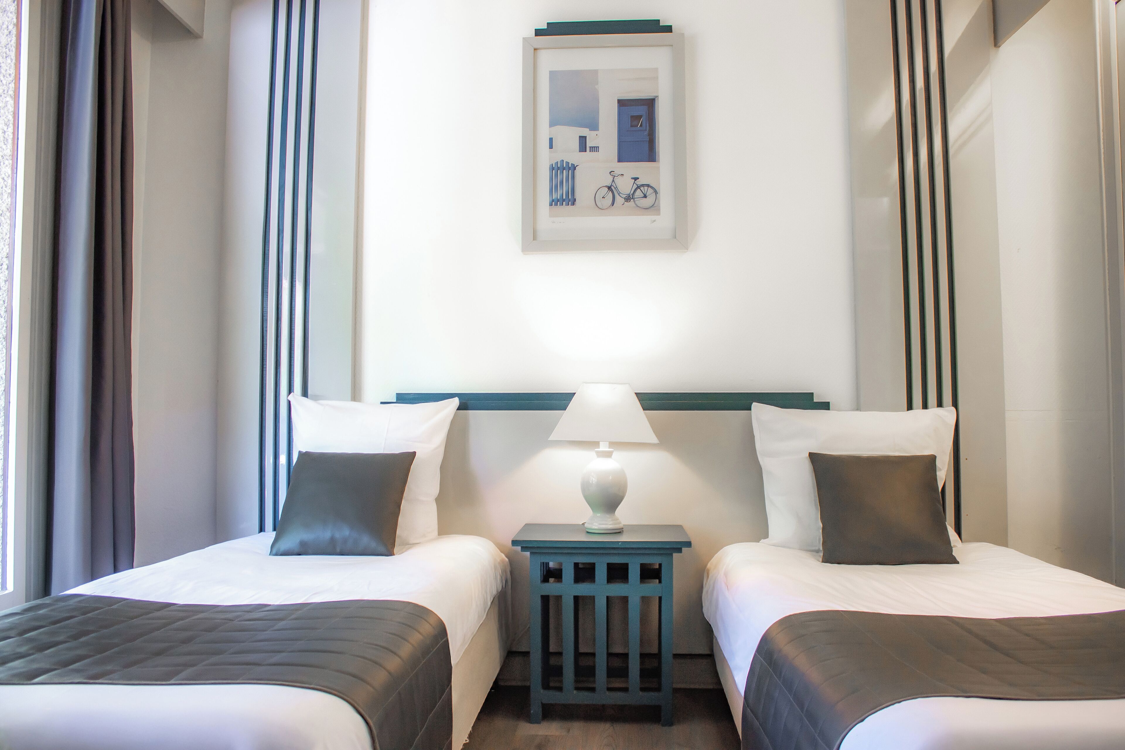Una camera d'albergo con due letti, un comodino con una lampada e un quadro appeso alla parete.
