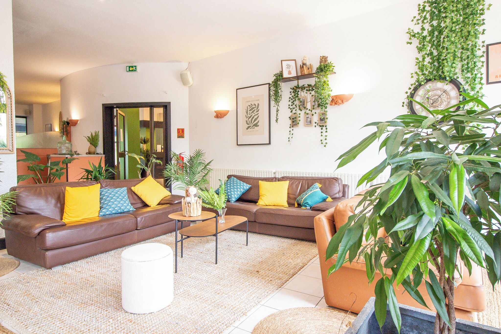 Een moderne woonkamer met een bruine bank, gele en blauwe kussens, een bijzettafeltje en verschillende planten.