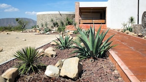 A modern building with a circular stone structure, a brick wall, and a paved walkway. - Termas De San Joaquin (Ramos Arizpe)