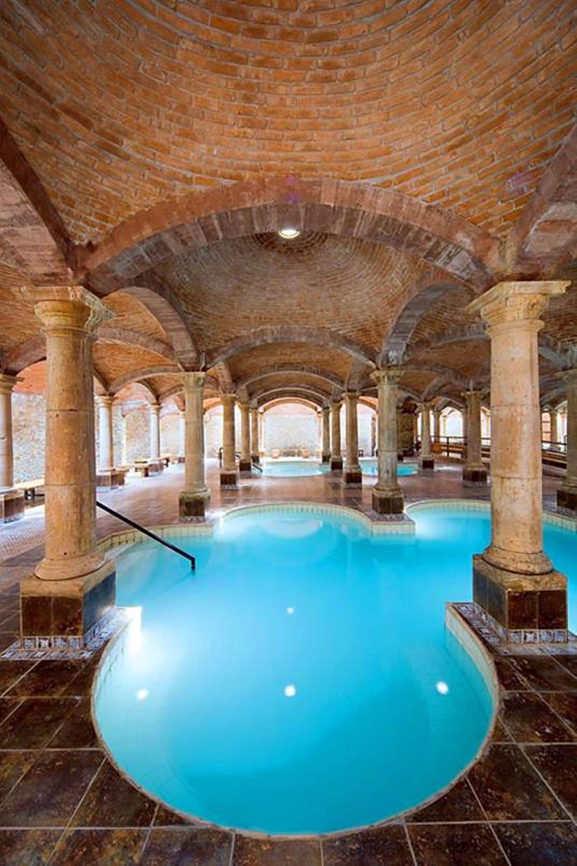 Una amplia piscina interior con techo de ladrillo y columnas.