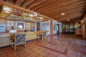 Un área de recepción con un mostrador de madera, dos sillas, piso de baldosas y techo de vigas de madera.