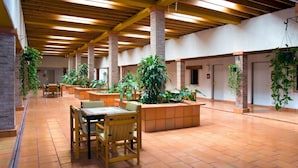 A spacious indoor area with wooden beams, brick pillars, and terracotta flooring. There are several wooden tables and chairs, and potted plants are placed around the room. - Termas De San Joaquin (Ramos Arizpe)