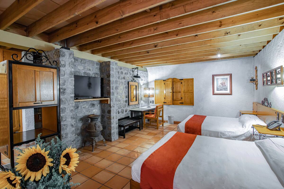 Una habitación con dos camas, una chimenea de piedra, armarios de madera, un televisor y una pequeña mesa con un teléfono.