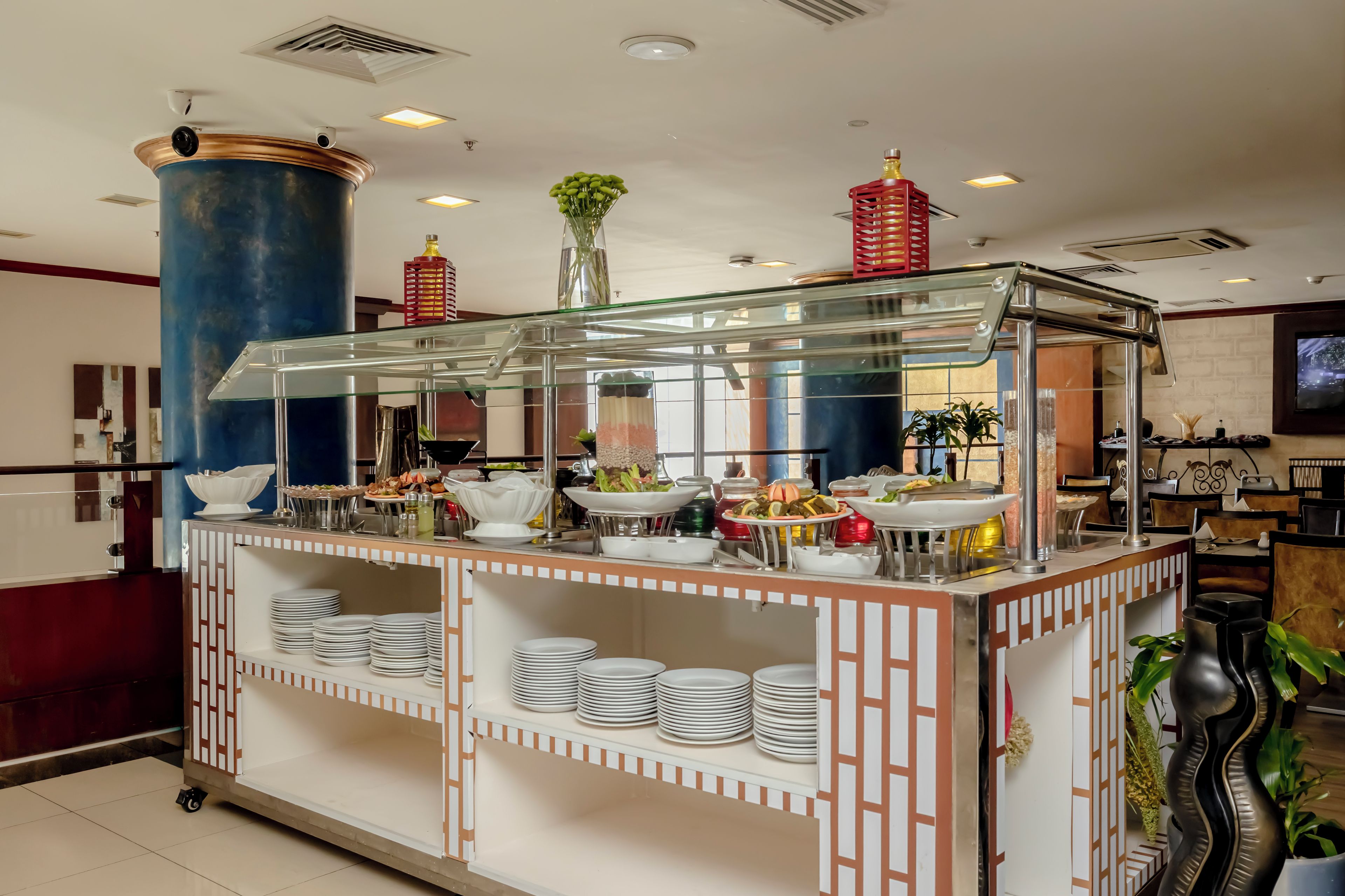 Disposição de buffet com estrutura de vidro, pratos e diversos alimentos.