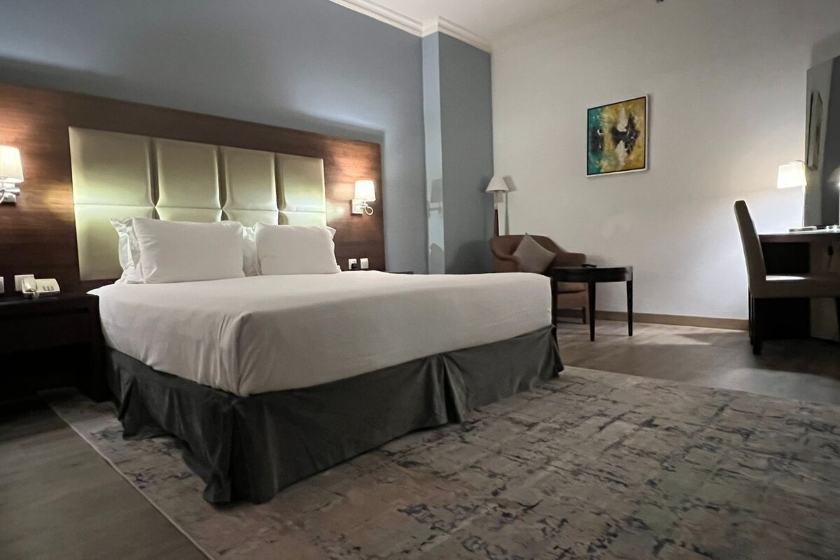 A hotel room with a large bed, bedside lamps, a desk, and a chair.