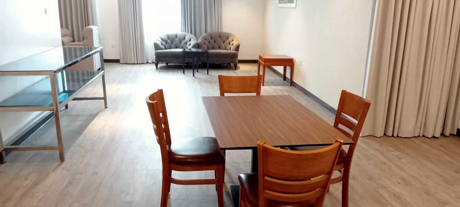 A dining area with a wooden table and chairs, a sofa, and a glass-top table.