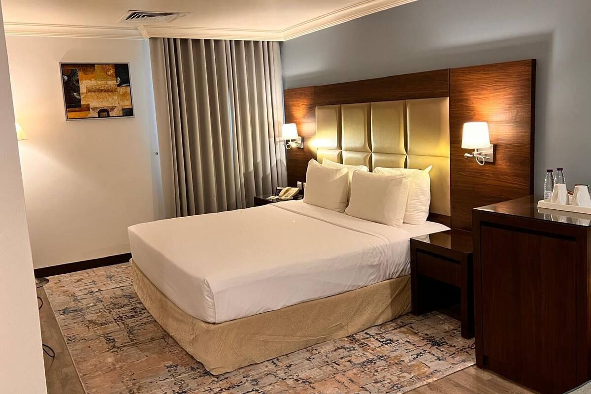 A hotel room with a large bed, bedside lamps, a wooden headboard, a desk, and a telephone.