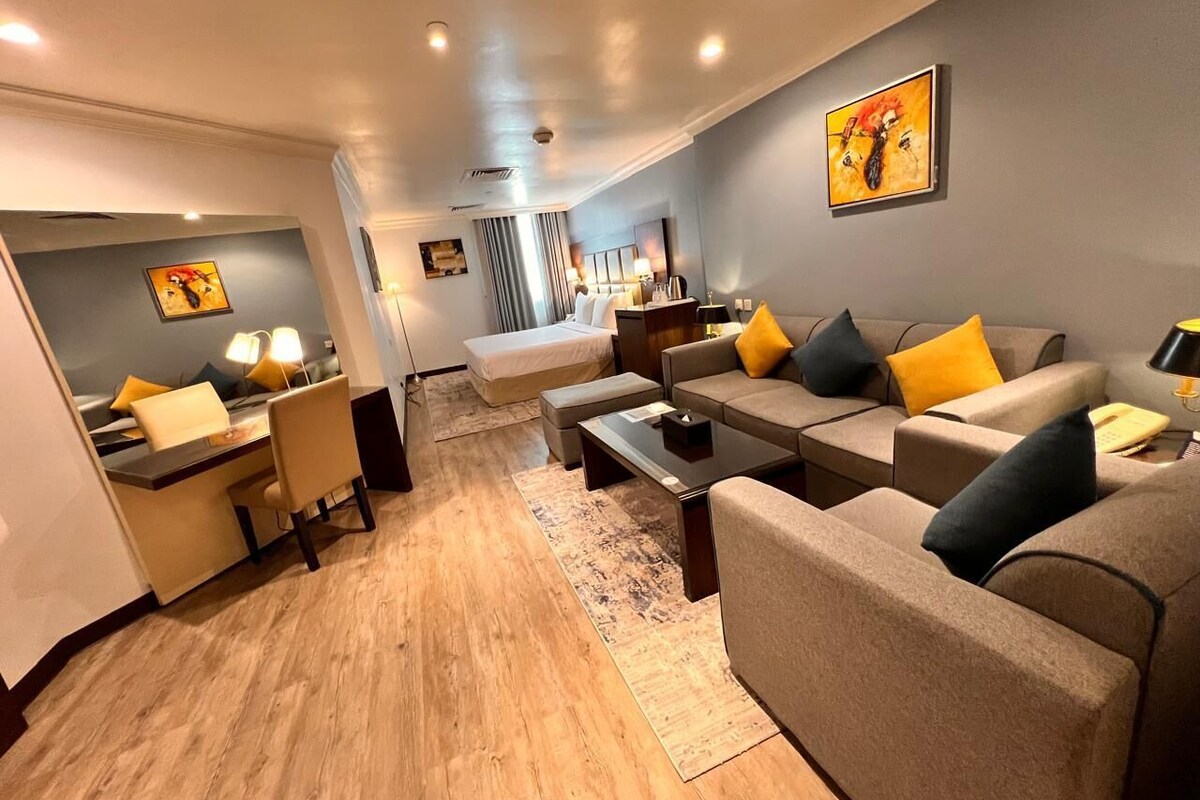 A modern hotel room with a sofa set, a dining area, and a bed.