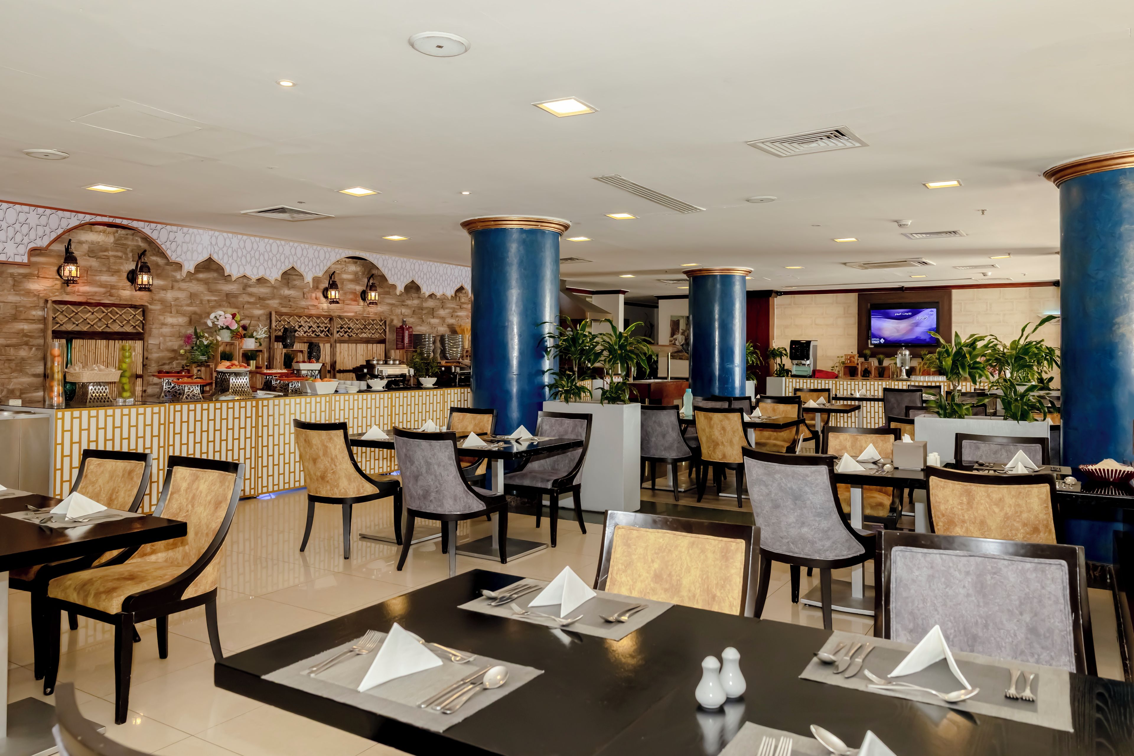A restaurant with multiple dining tables and chairs, a bar area, and a television screen.