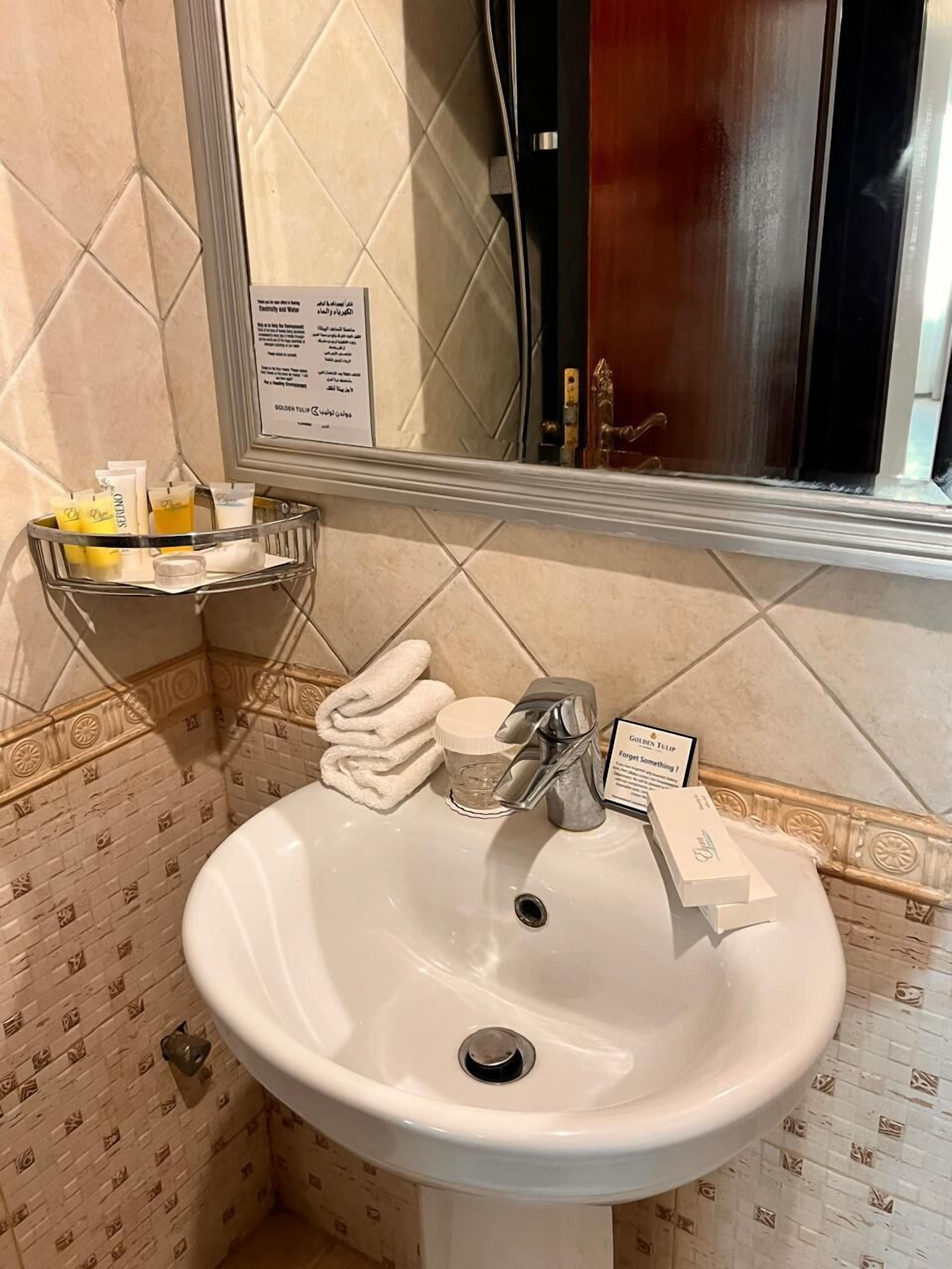 A bathroom with a white sink, a mirror, a towel rack with folded towels, and a sign on the wall.