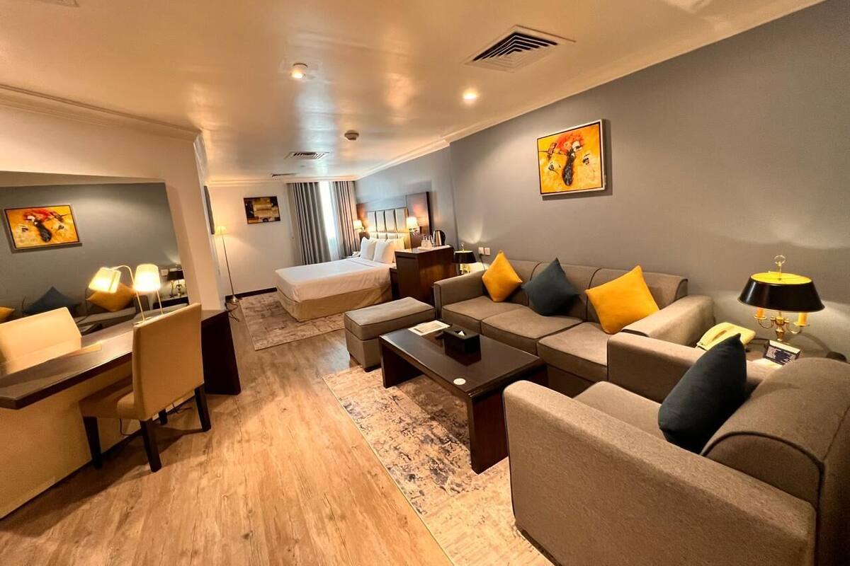 A modern hotel room with a bed, sofa, coffee table, desk, and lamp.