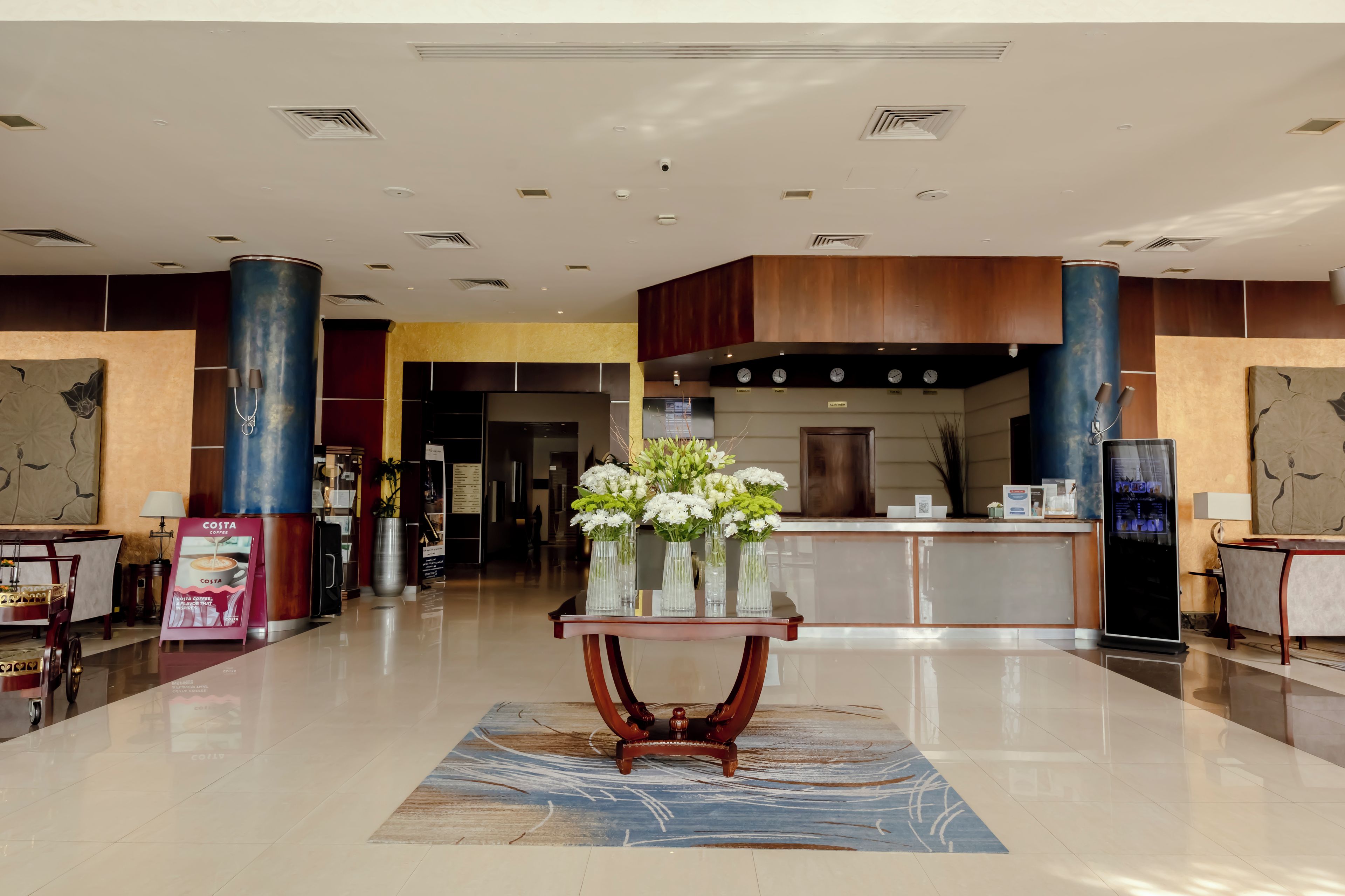 A hotel lobby with a reception desk, a coffee station, and a decorative table with vases.