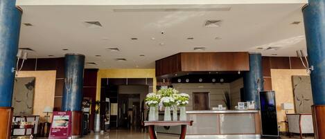 A hotel lobby with a reception desk, framed portraits above, and a coffee station.