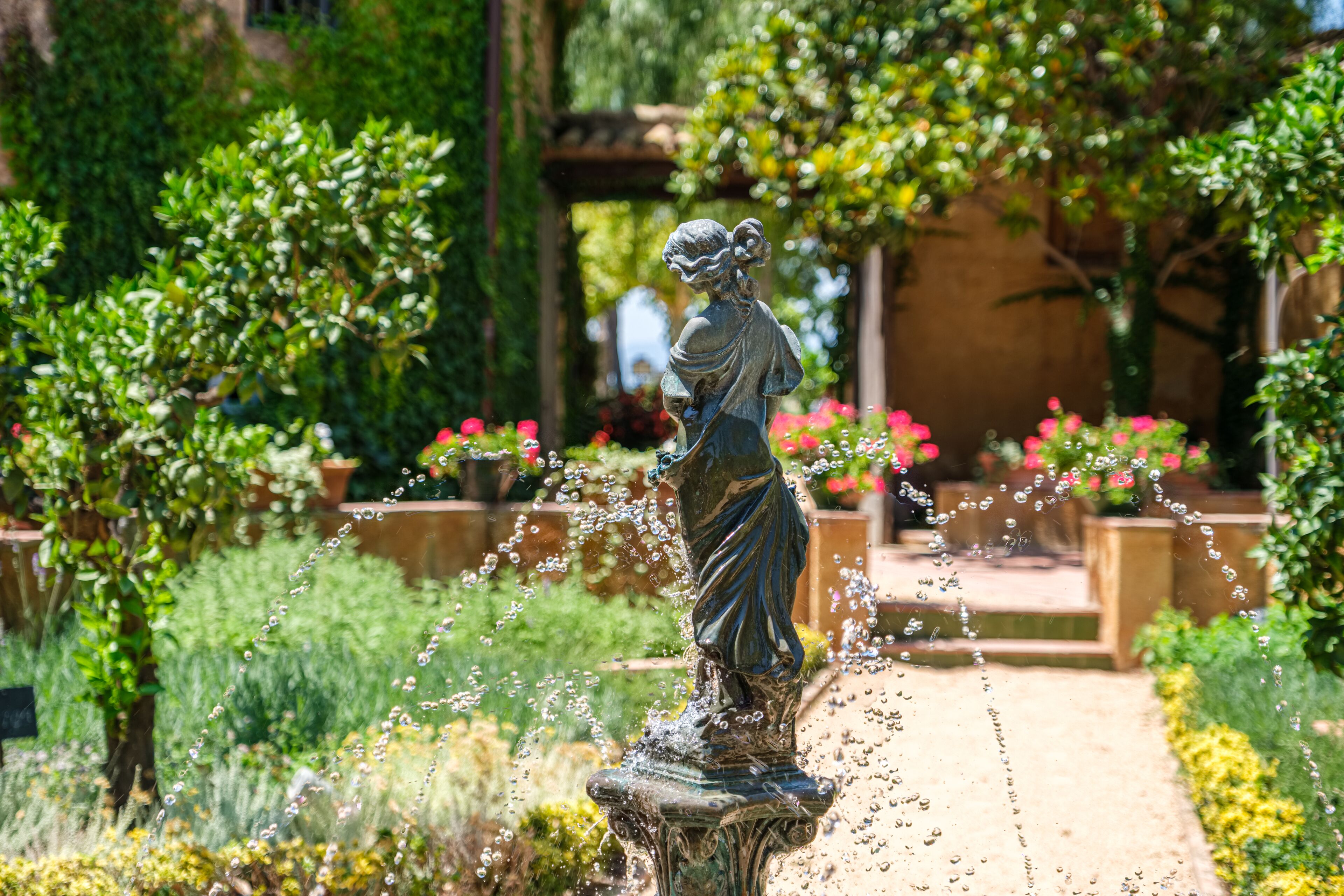 A statue in a garden with water features and greenery.