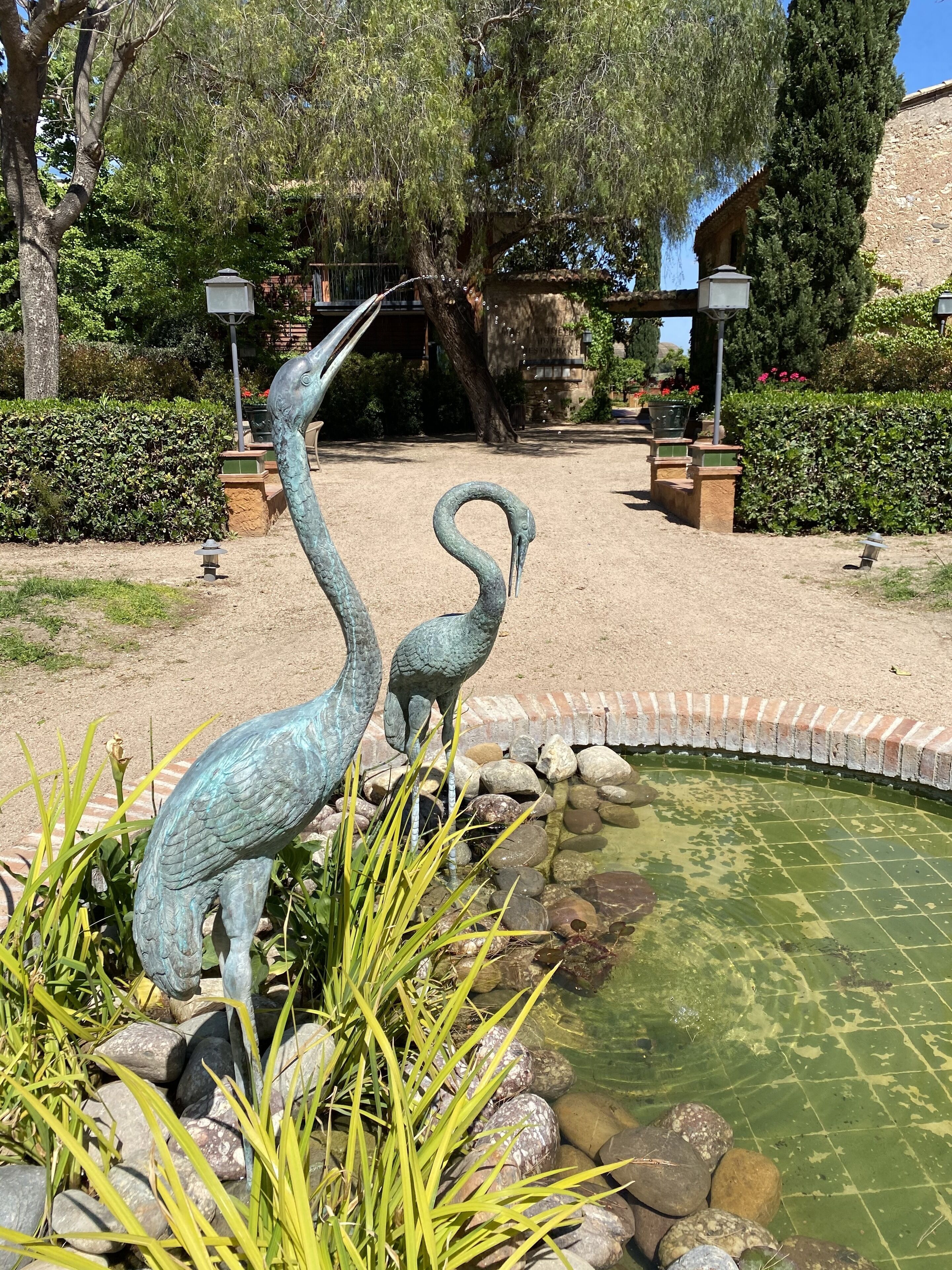 A garden with two large bird sculptures, a pond, and a brick pathway.