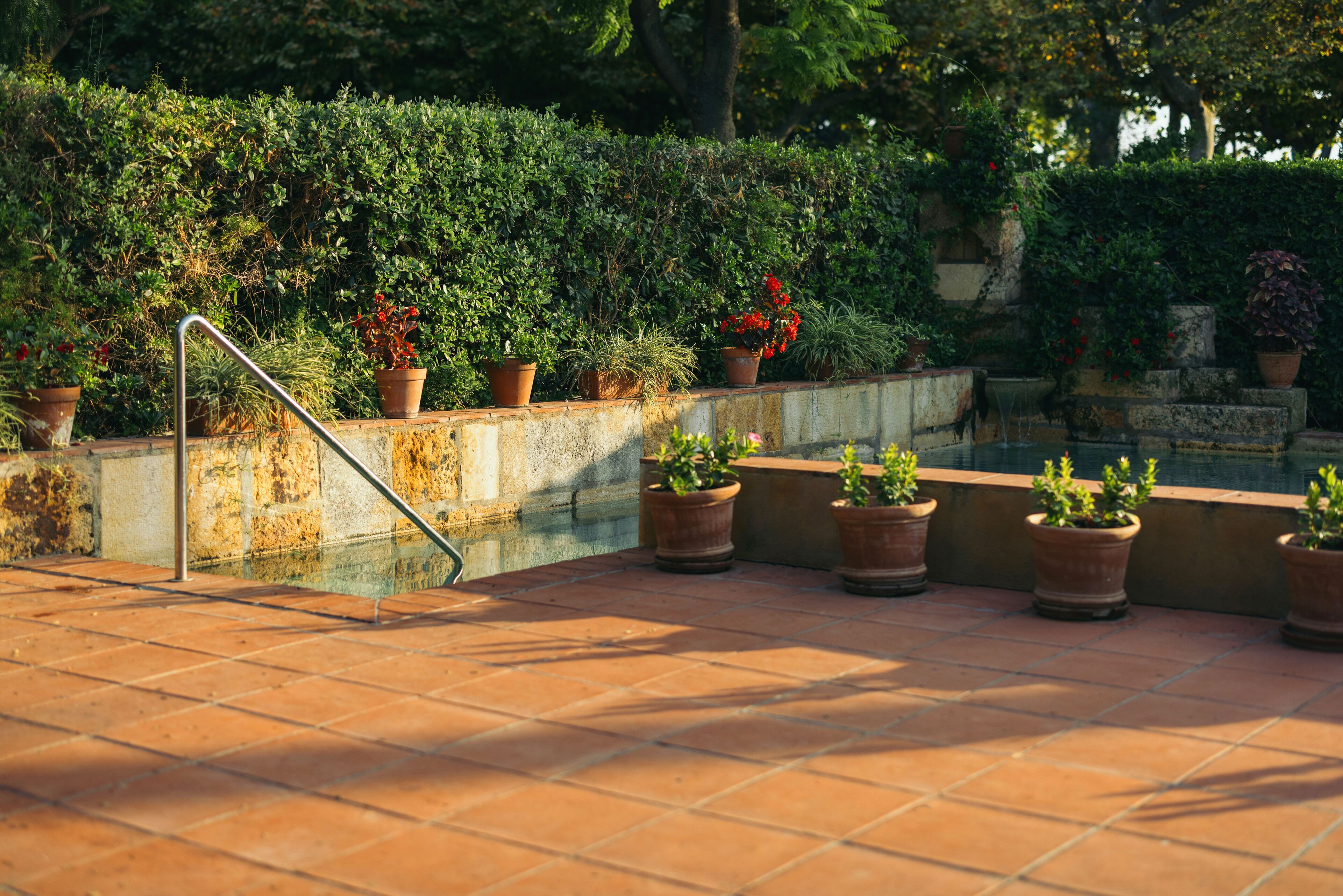 A terracotta-tiled patio with potted plants and a metal handrail.