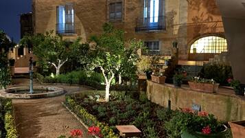 Un edificio histórico con un patio que presenta una fuente, plantas en macetas y un sendero.