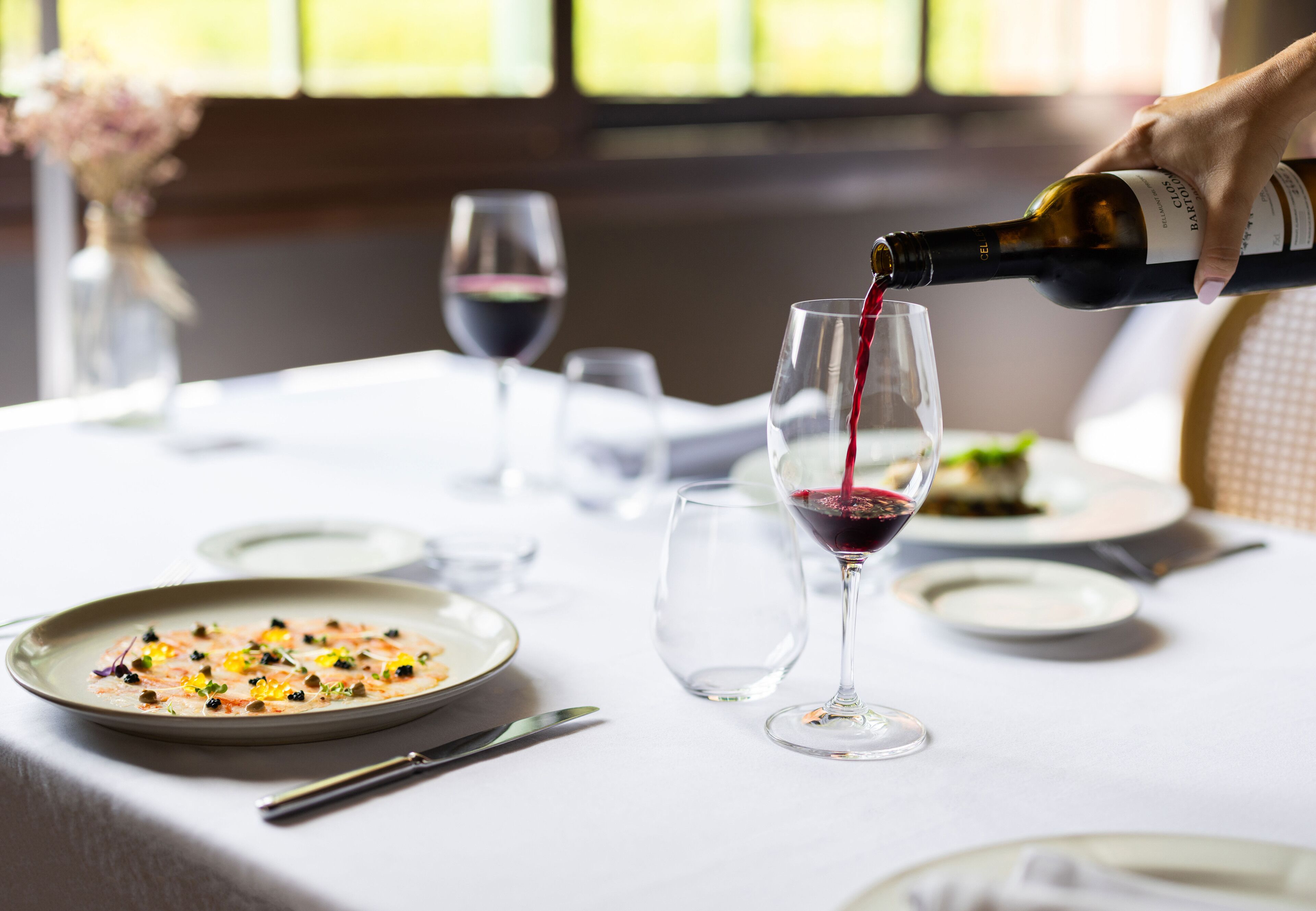 A table set for dining with a bottle of wine being poured into a glass.