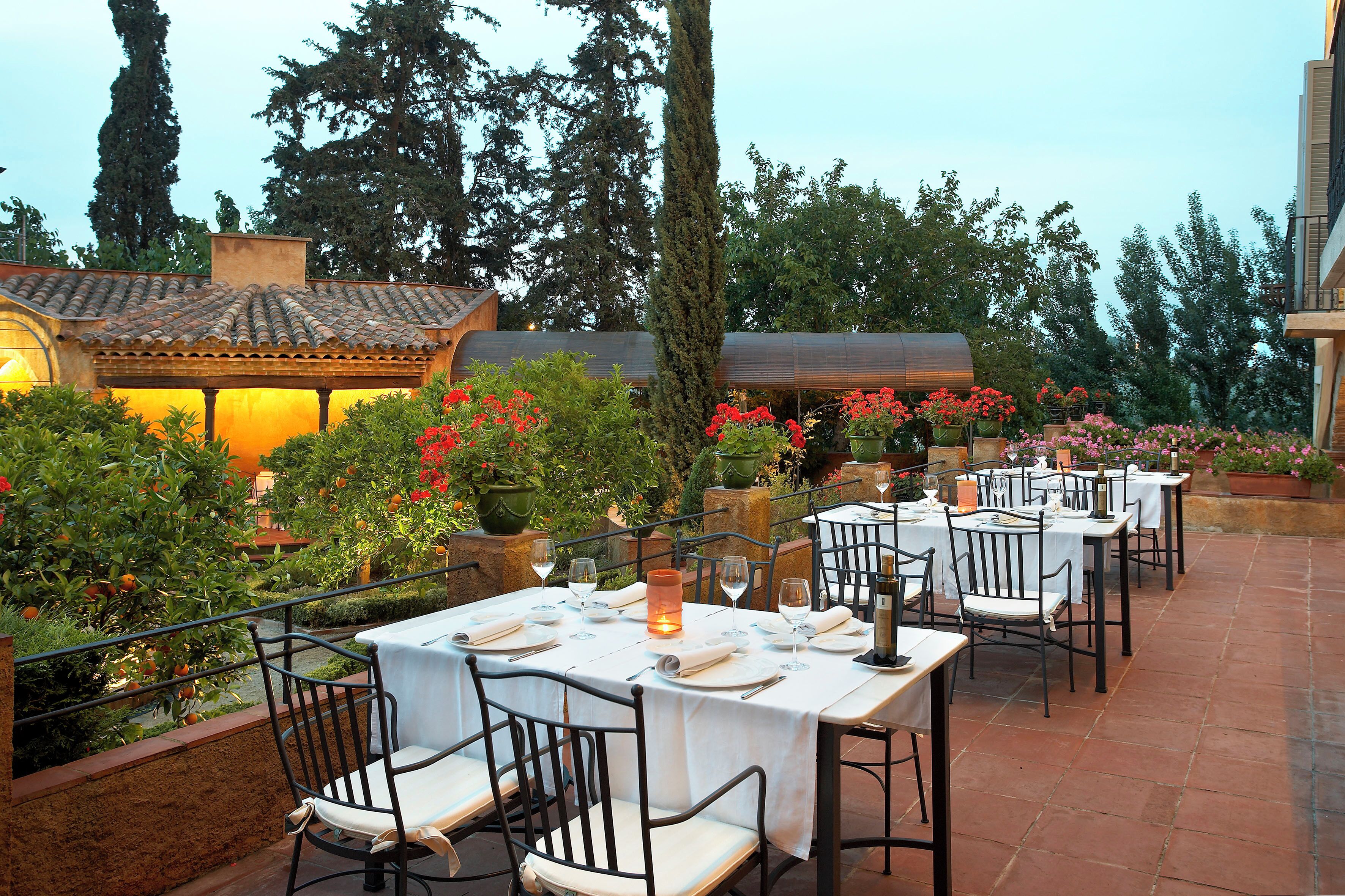 An outdoor dining area with tables and chairs, surrounded by potted plants and trees.