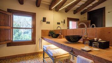 A bathroom with a large window, wooden beams, a sink with a bowl, and a bench.