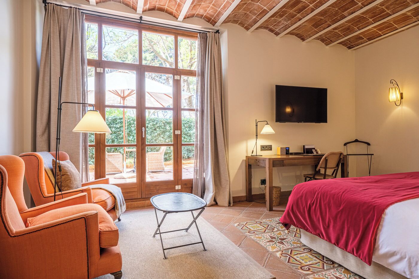 Hotelkamer met een bed, een bureau, een televisie en een zithoek met een stoel en een klein tafeltje.