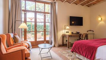 Hotelkamer met een bed, een bureau, een televisie en een zithoek met een stoel en een klein tafeltje.