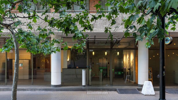 A hotel entrance with glass doors, a white bollard, and a tree in the foreground.