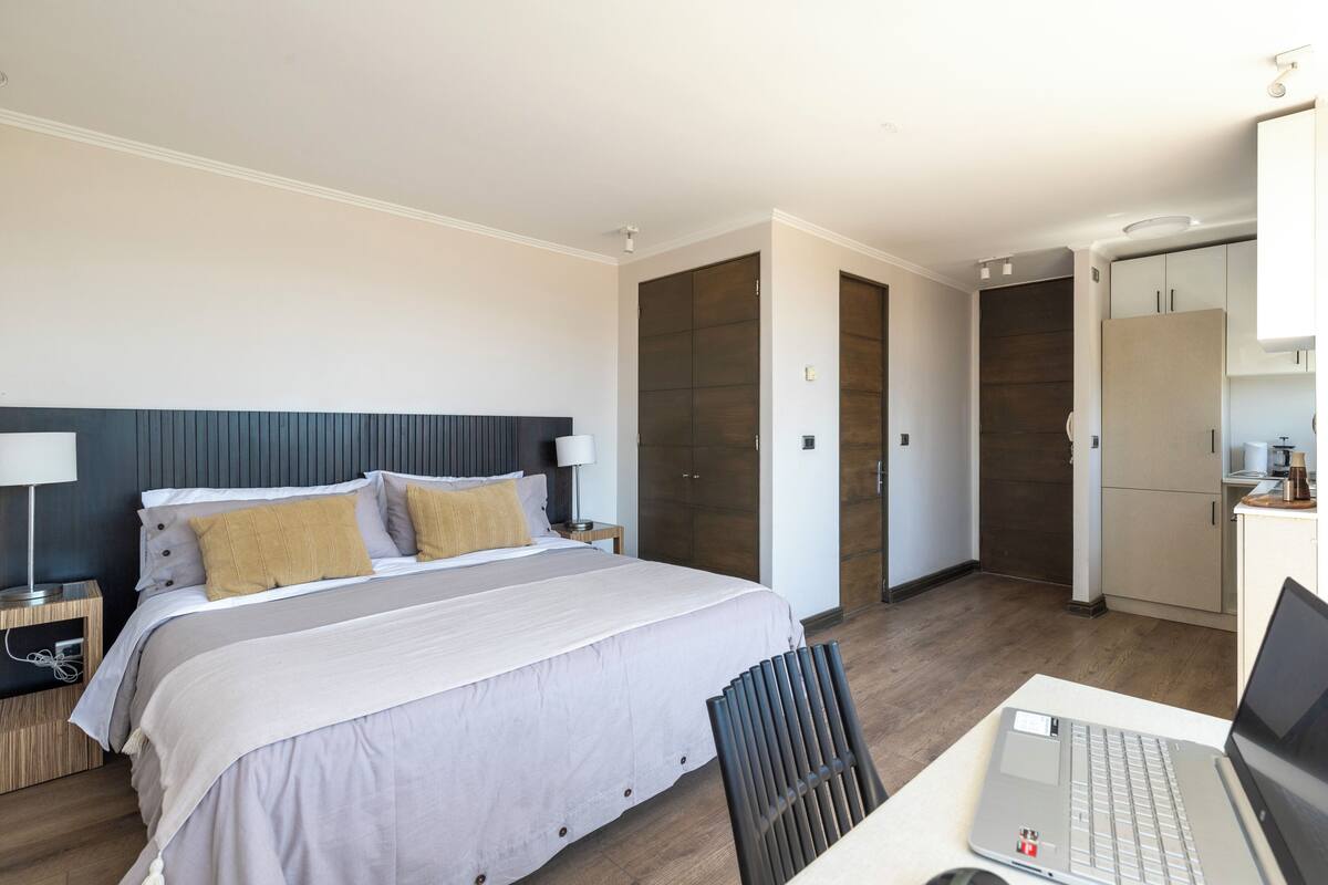 Ein modernes Hotelzimmer mit einem aufgeräumten Bett, einem Laptop auf einem Schreibtisch und einem Kleiderschrank.
