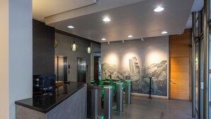 A modern reception area with a black reception desk, turnstiles, and a wall-mounted security camera.