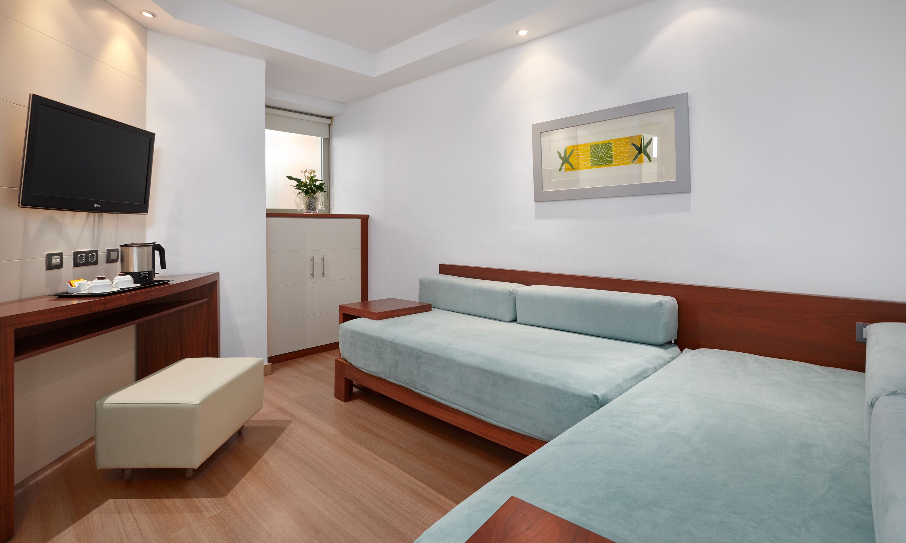 A modern hotel room with a bed, a desk with a coffee maker, a TV, and a cabinet.