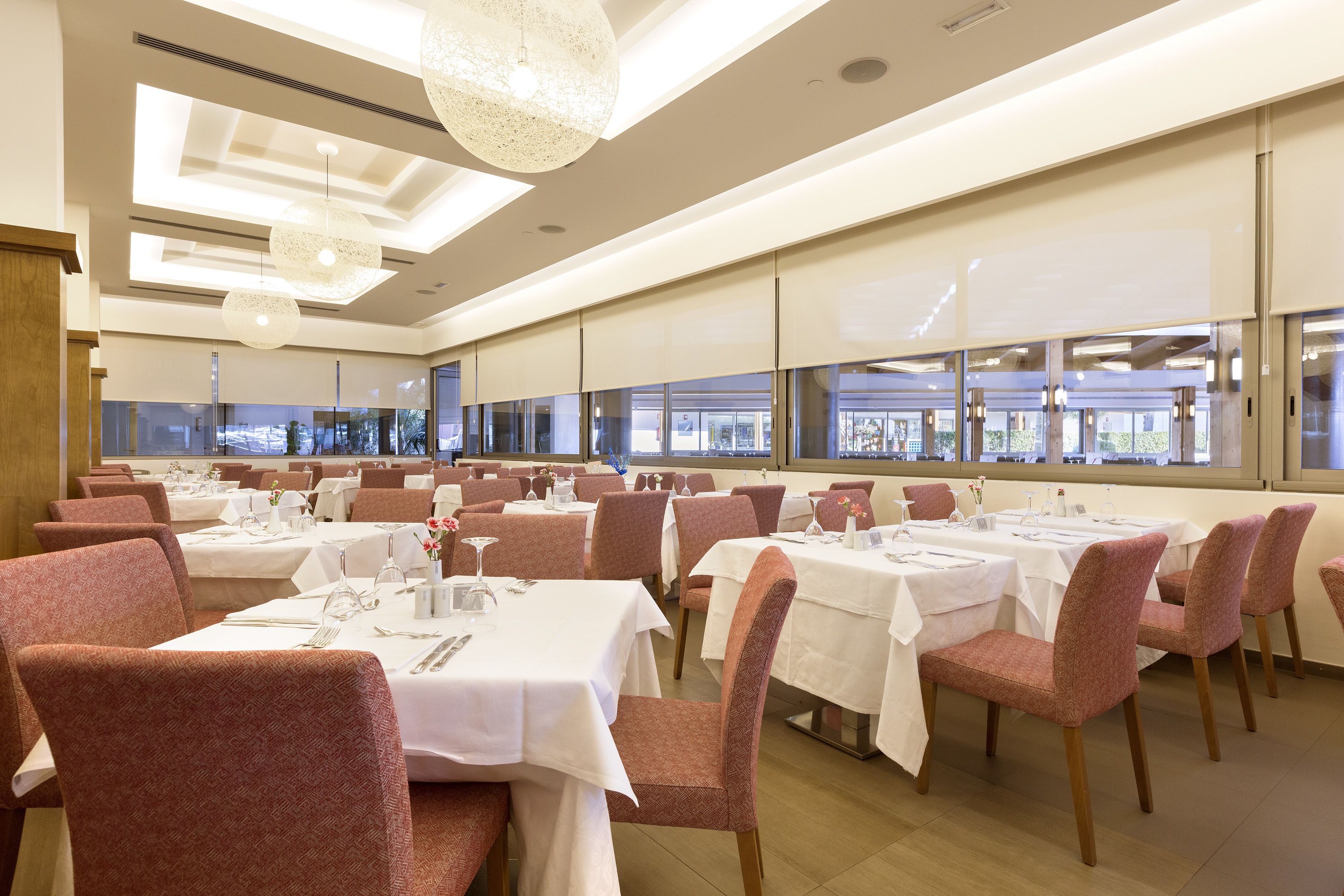 Un restaurante con varias mesas y sillas, ventanas amplias y un diseño moderno en el techo.
