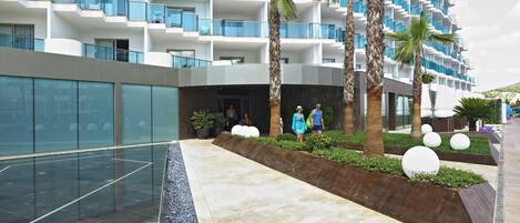 A modern hotel with multiple balconies, a swimming pool, and palm trees.