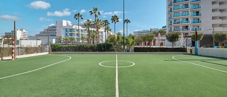 A soccer field with goalposts and a net, surrounded by palm trees and buildings.