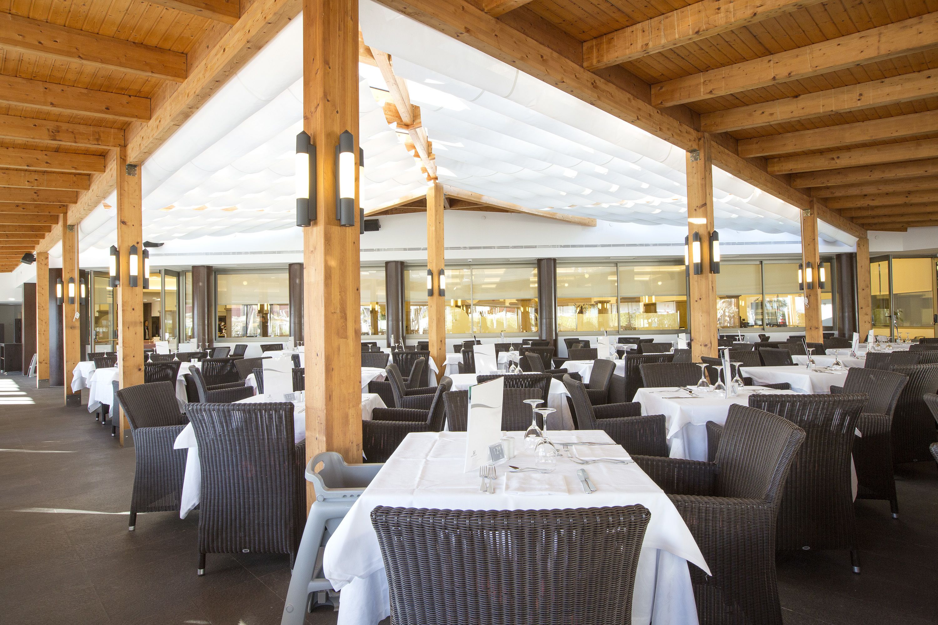 An outdoor restaurant with wooden beams, wicker chairs, and tables set for dining.