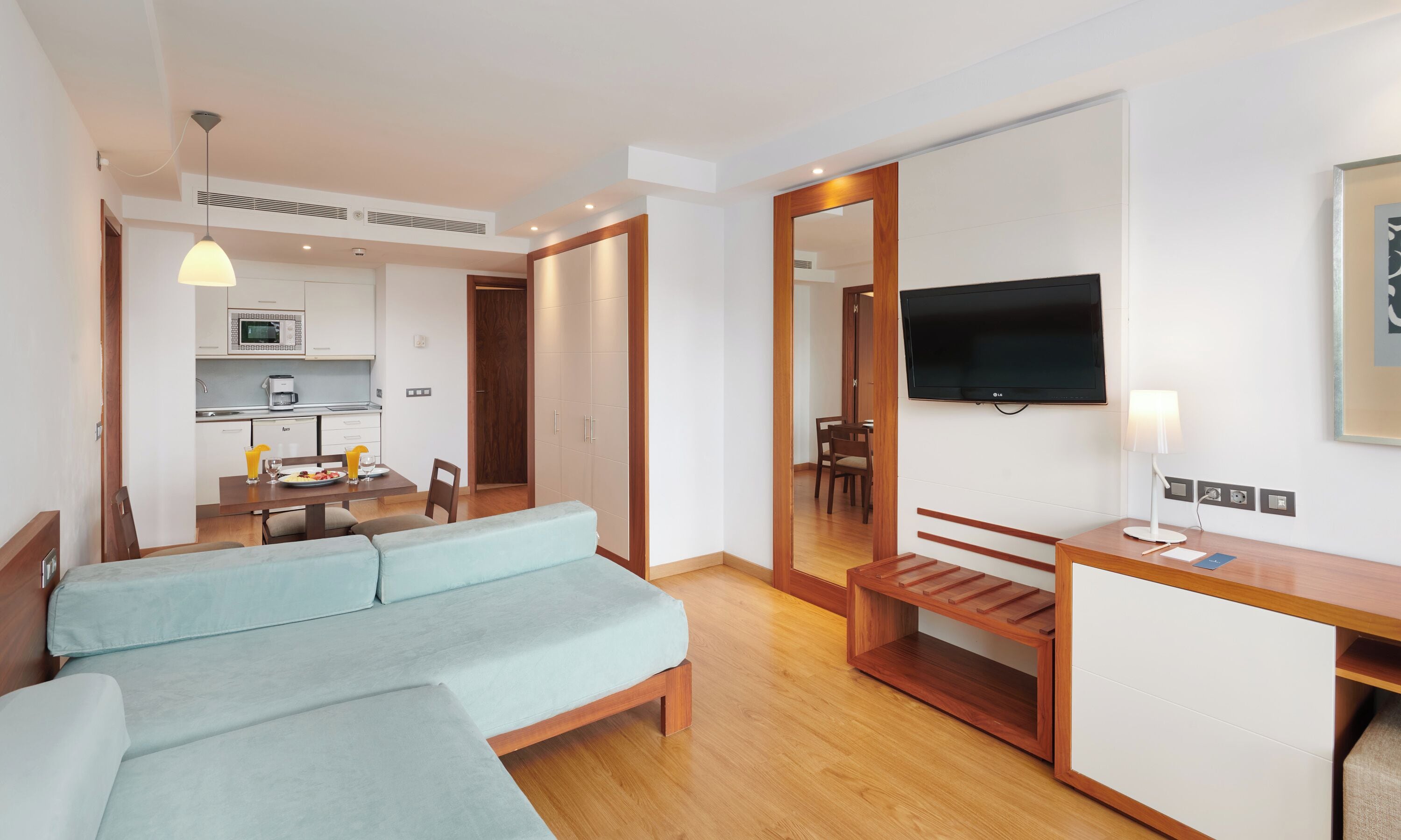 Habitación de hotel moderna con sofá, escritorio, televisión y kitchenette.