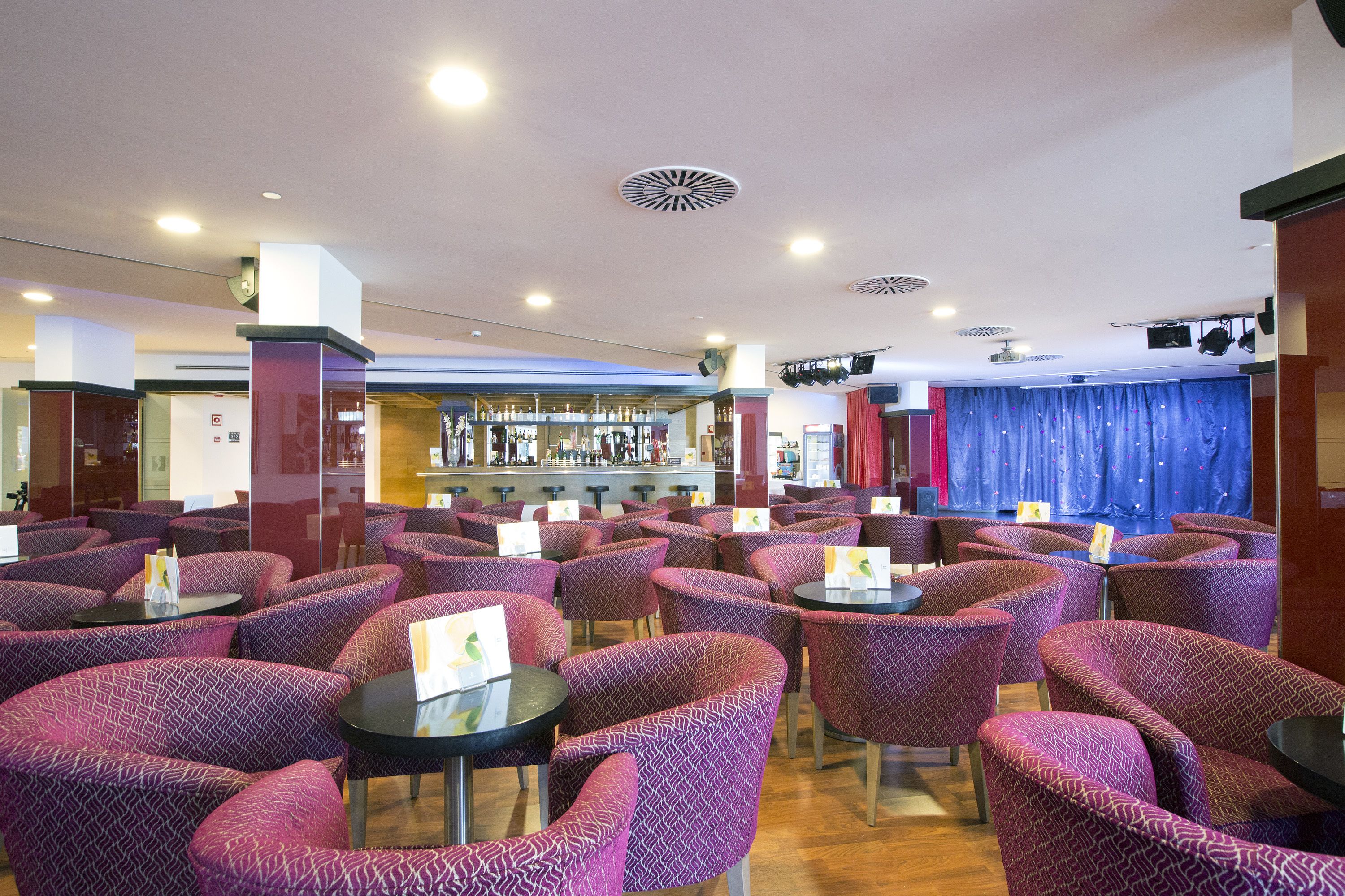 Un ristorante con sedie e tavoli a motivi viola, un'area bar sullo sfondo e una tenda blu.