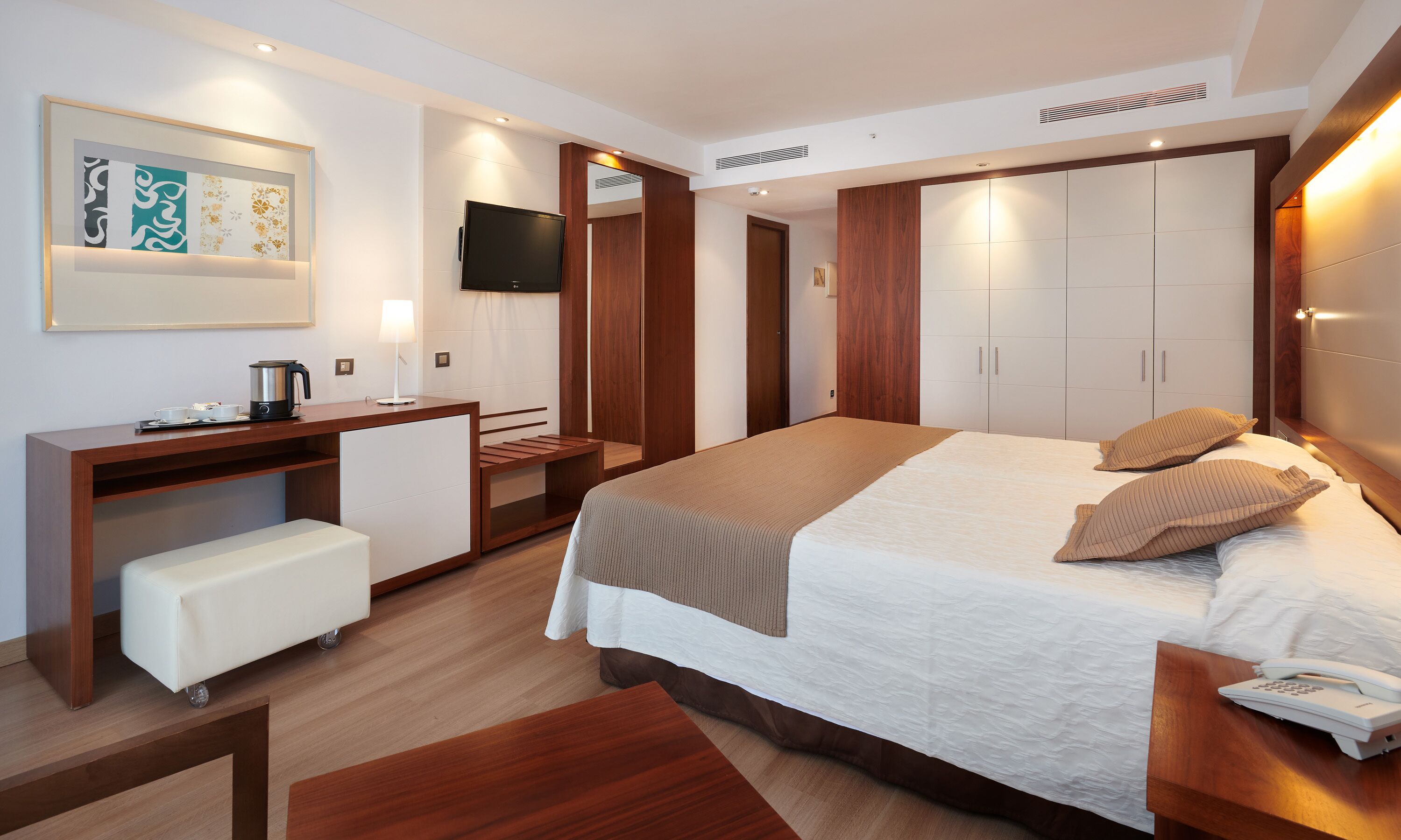 A modern hotel room with a bed, bedside table, desk, chair, and a television.