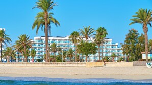 Een strandhotel met meerdere balkons, palmbomen en een zandstrand.