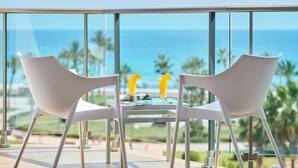 Een balkon met twee witte stoelen en een tafel, met uitzicht op een strand met palmbomen en de oceaan.