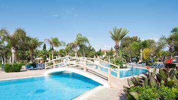 Relax by the resort pool surrounded by lounge chairs and umbrellas, with a wooden bridge and palm trees nearby.