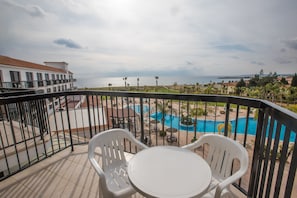 A balcony with white plastic chairs and a table, overlooking a swimming pool and a view of the sea. - Nelia Sea Breeze (Ayia Napa)