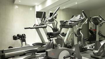 Un gimnasio con varias máquinas de ejercicio, incluyendo cintas de correr y bicicletas estáticas, y una televisión montada en la pared.