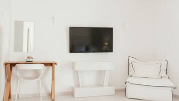 A minimalist room with a wooden desk, a white chair, a white bench, and a white bed with black piping.