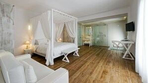 Une chambre d’hôtel moderne avec un lit à baldaquin, un coin salon avec un banc, une petite table et un téléviseur.