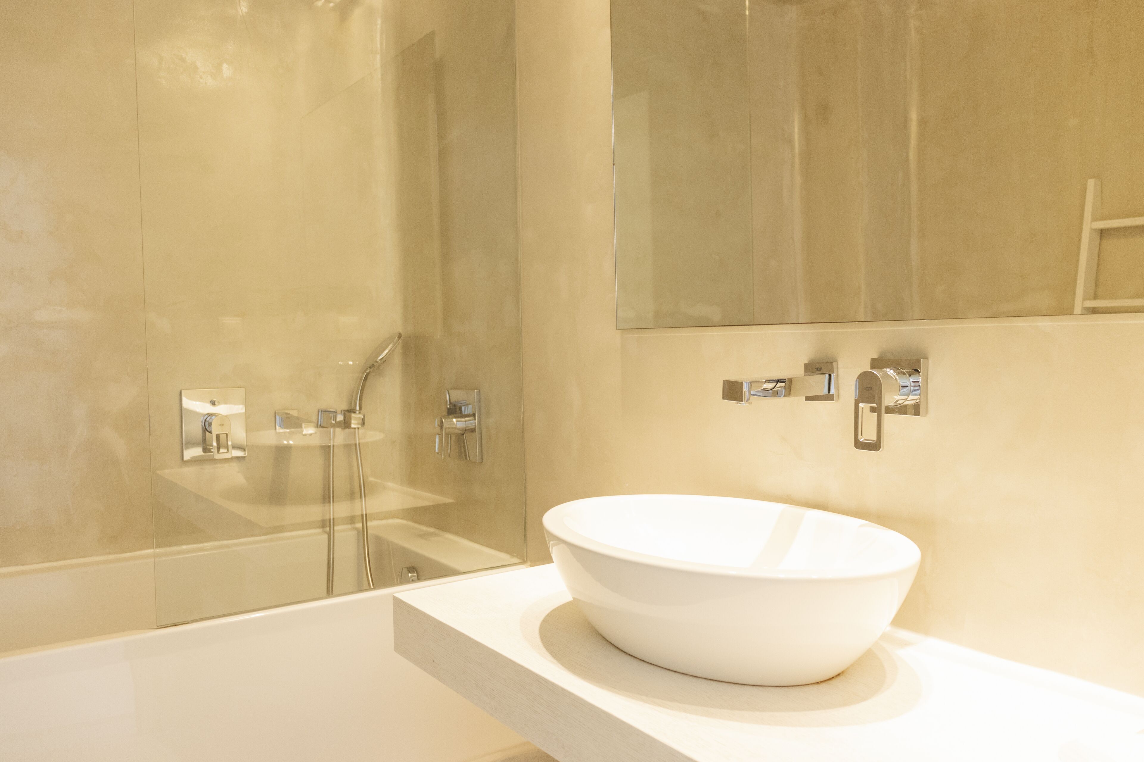 A modern bathroom with a large white sink, a glass shower enclosure, and a mirror above the sink.