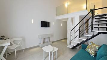 A modern living room with a staircase, a flat-screen TV, a dining area with chairs, and a sofa with a floral cushion.