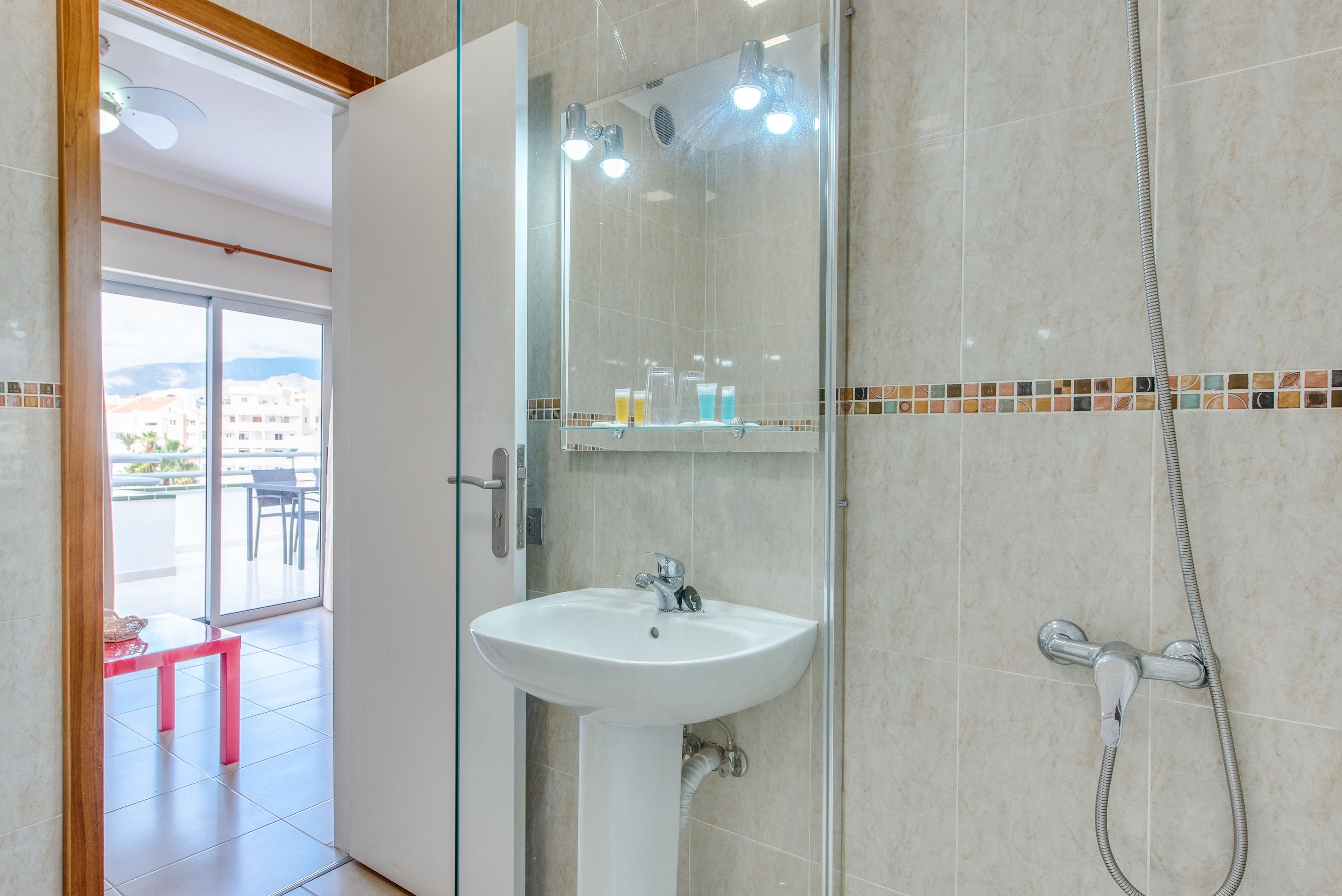 Une salle de bain avec une douche à parois de verre, un lavabo blanc et une zone de douche carrelée.